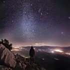 Starry night beach scene with Milky Way, cabin, and river