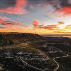 Colorful countryside scene with sunset sky, swirling clouds, houses, and ocean view.