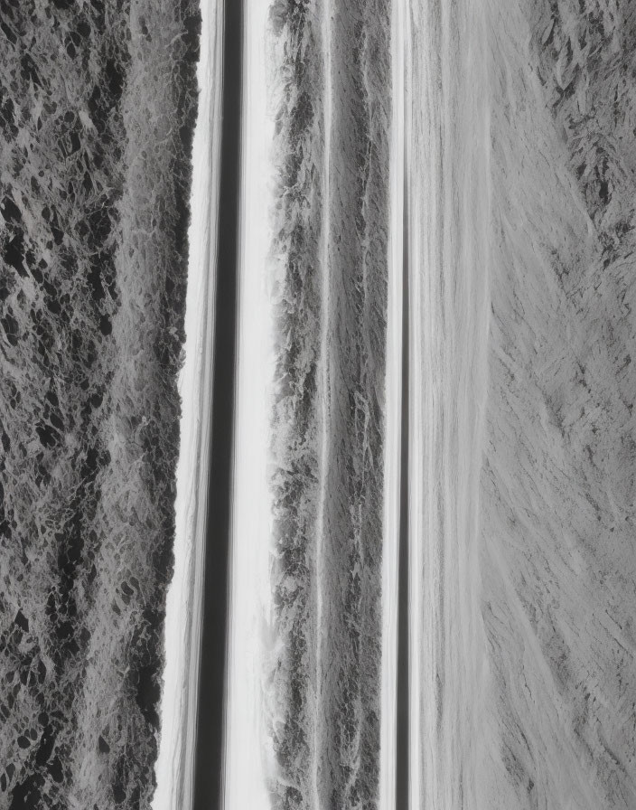 Snow-covered road surrounded by trees in aerial view