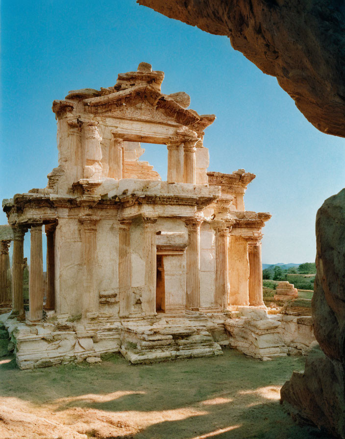 Classical temple ruins with Corinthian columns framed by cave entrance