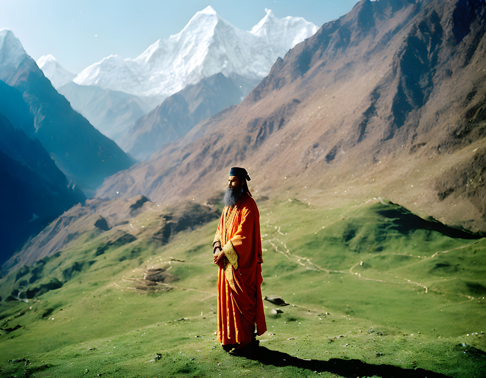 Bearded man in orange robes against mountain backdrop