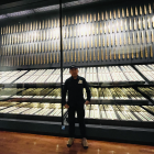 Person in Cap and Jacket Viewing Illuminated Swords Display in Modern Room