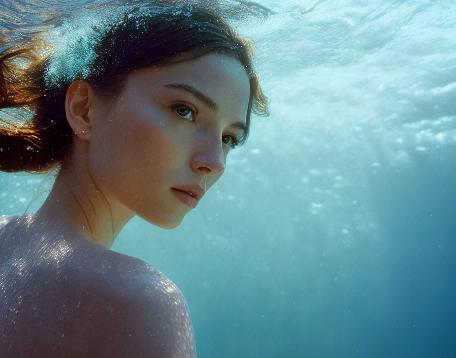 Young woman submerged in clear blue water with air bubbles and serene expression