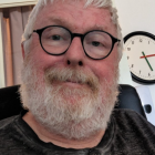 Elderly man smiling with white beard and glasses near clock building.