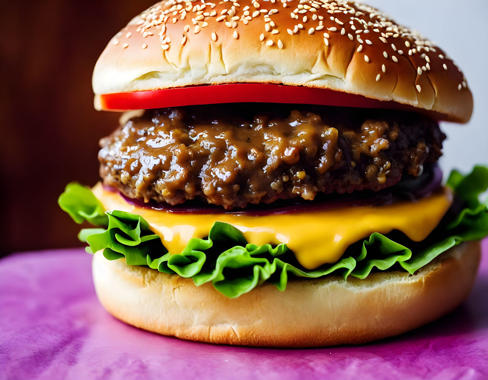 Close-up of cheeseburger with lettuce, cheese, beef patty, sauce on sesame seed bun on