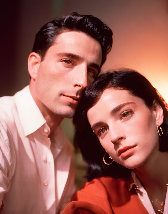 Man and woman posing intimately in white and orange outfits against warm backdrop