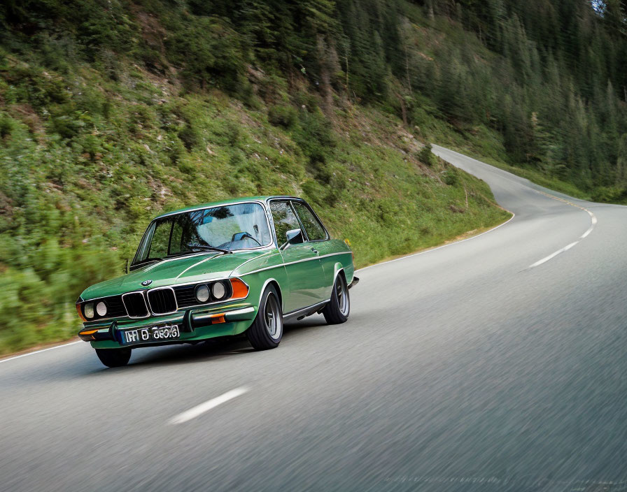 Vintage green BMW 2002 on winding mountain road with trees