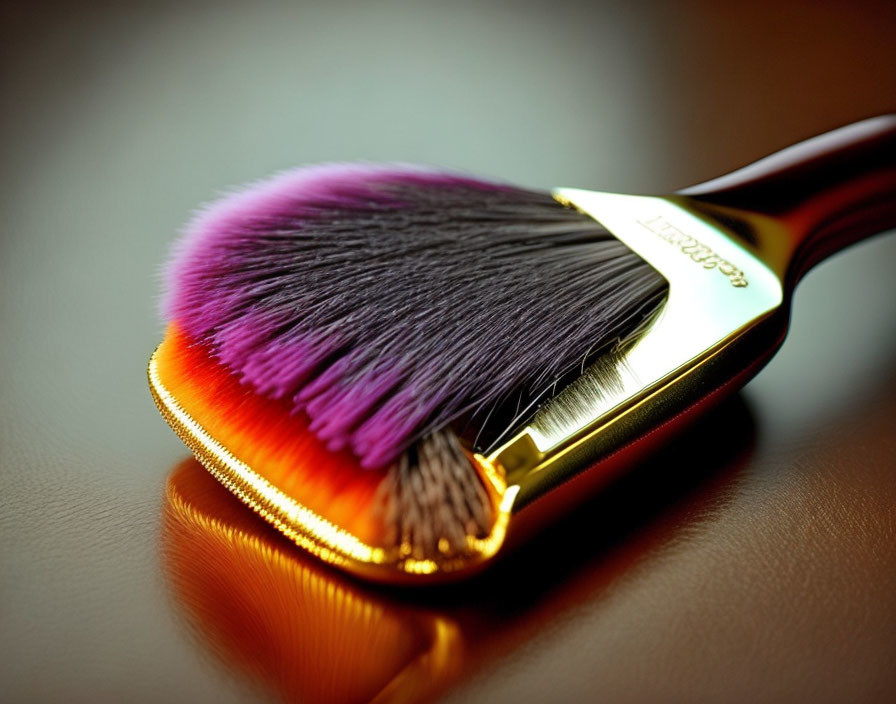 Makeup brush with purple to pink bristles on golden surface