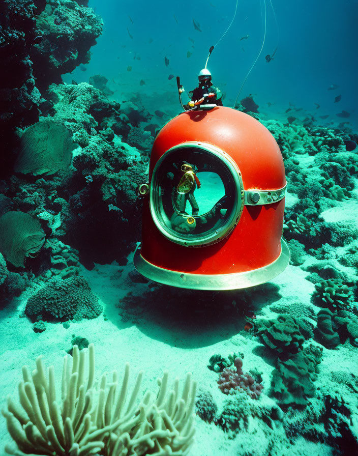 Red submarine with large front window on coral seabed with diver and marine life.