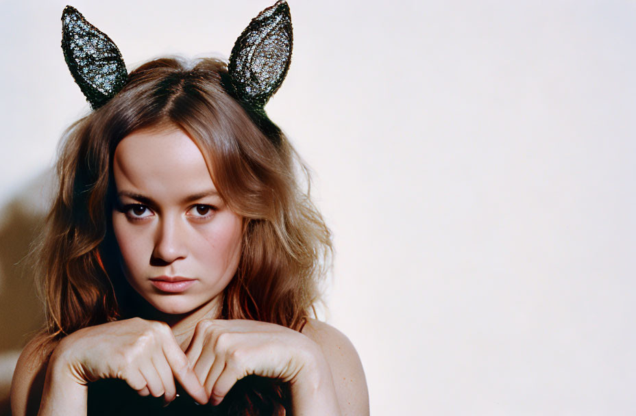 Serious woman with sparkly cat ears on beige background