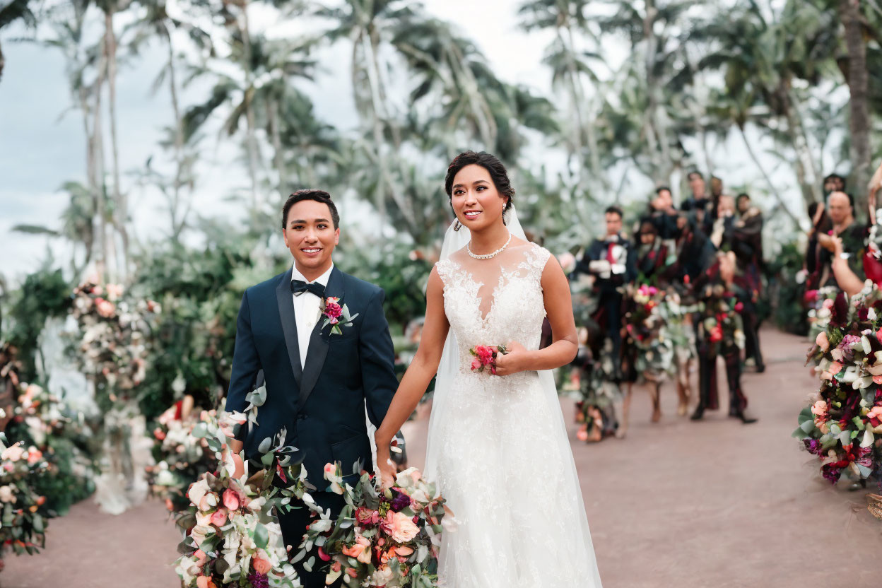 Newlywed couple walking down outdoor aisle with guests and palm trees