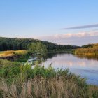 Tranquil countryside landscape with river, wildflowers, fence, and distant church