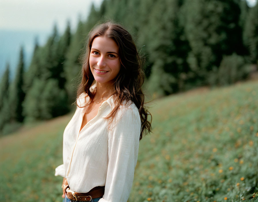 Smiling woman in white blouse in sunny meadow with trees