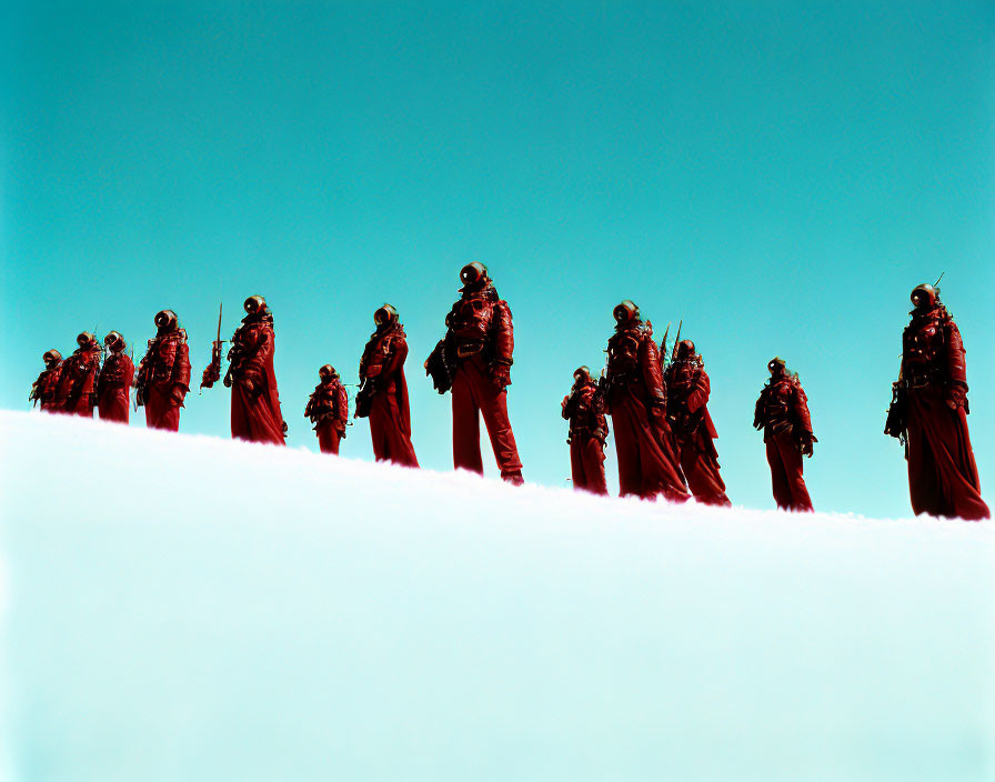 Group of people in red suits trekking snowy slope under clear sky