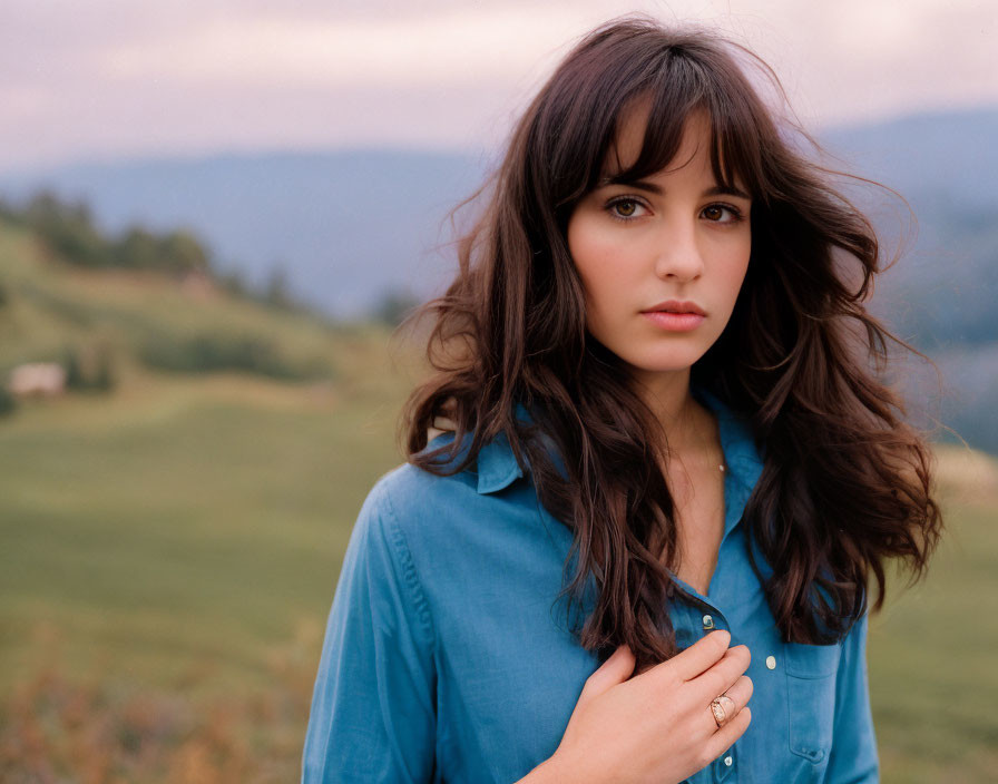 Dark-haired woman in blue shirt standing in field with mountains