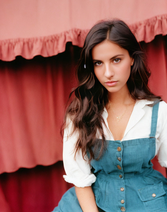 Young woman with long brown hair in white blouse and teal jumper against crimson backdrop