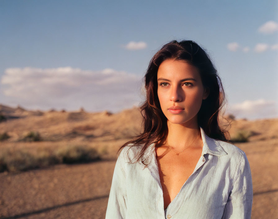 Dark-haired woman in light blue shirt contemplates desert horizon under clear sky