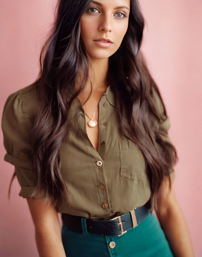 Woman with long brown hair in olive green blouse and teal skirt on pink background