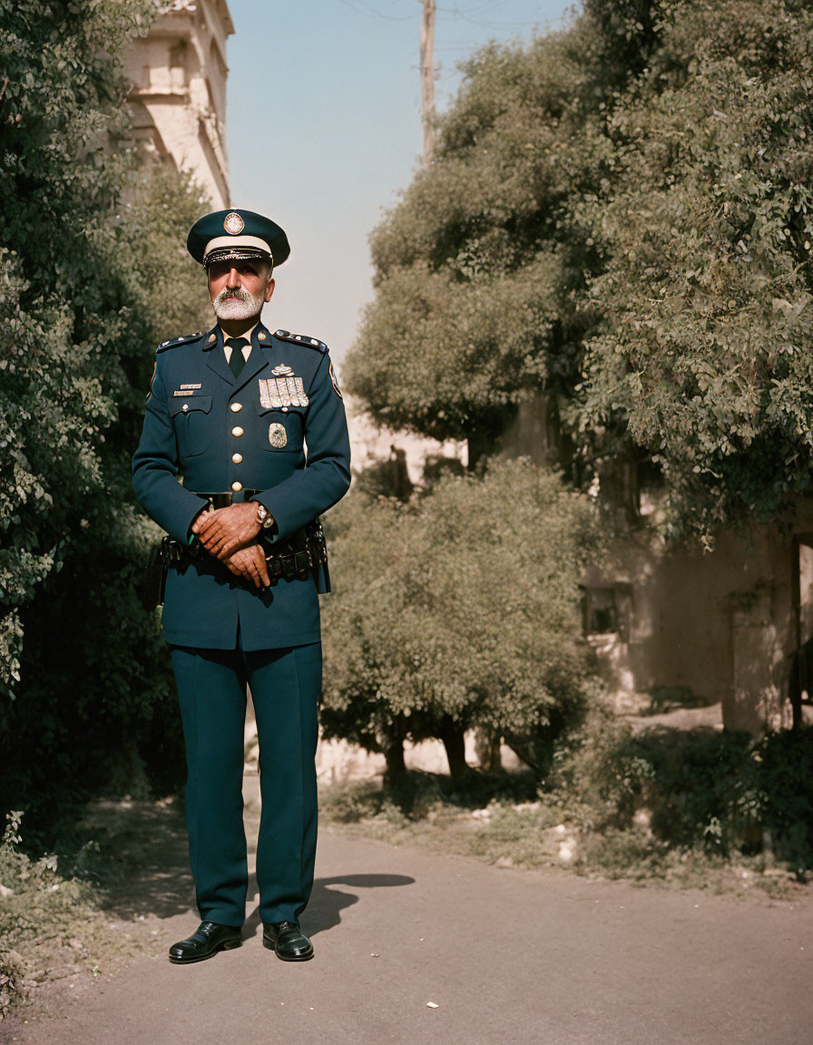 Decorated police officer with peaked cap and mustache standing confidently outdoors.