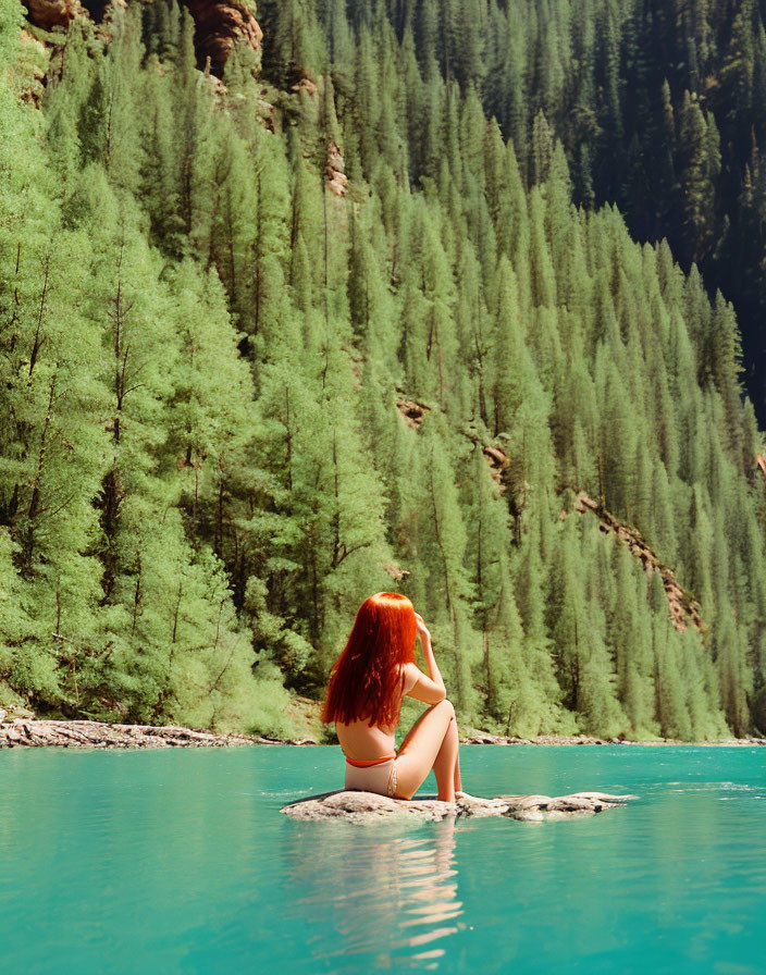 Red-haired woman by turquoise lake with pine trees and clear sky