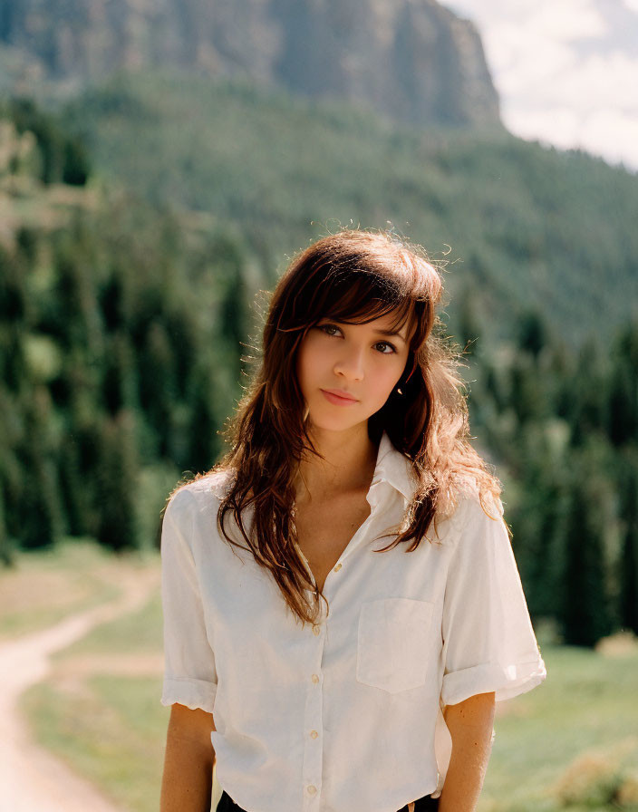 Brown-haired woman in white shirt against pine forest and mountains backdrop