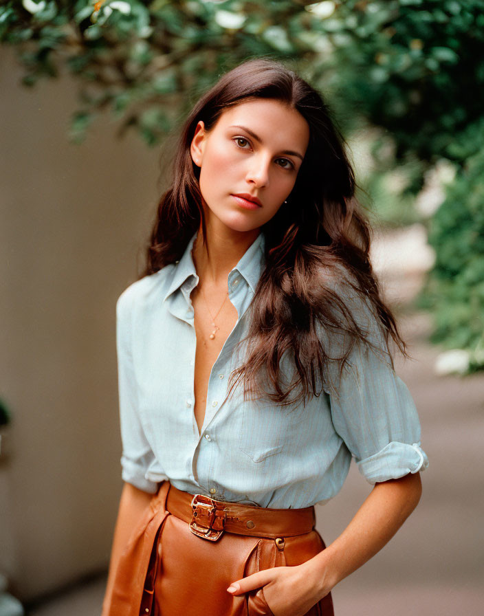 Long-haired woman in light blue shirt and brown belt posing thoughtfully