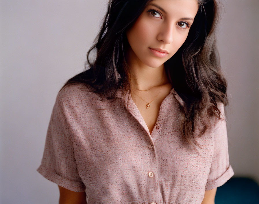 Dark-haired woman in pink shirt and necklace on neutral backdrop