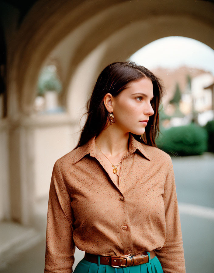 Dark-haired woman in polka-dot blouse and teal skirt against arched backdrop