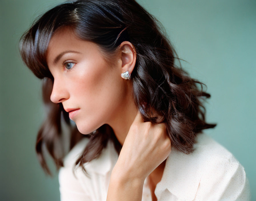 Woman with short brown hair in white blouse and earring gazes away.