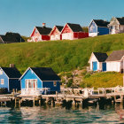 Vibrant waterfront houses with jetty, grassy hill, and blue sky