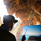 Artist painting seaside landscape in cave with sky and sea view