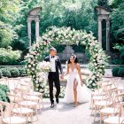 Wedding couple holding hands under sunflower archway in warm sunlight