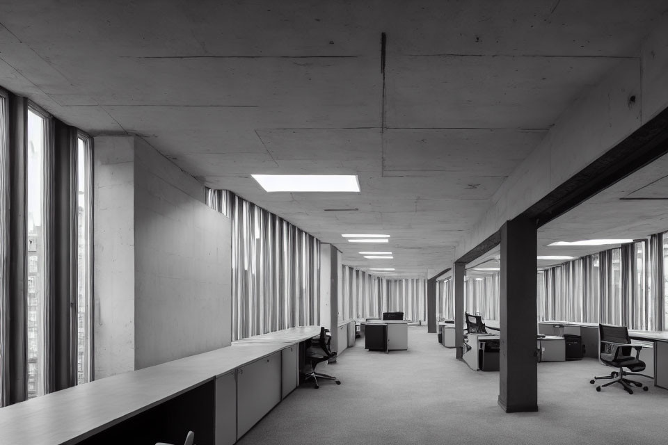 Modern monochrome office interior with empty desks, concrete pillars, and large windows