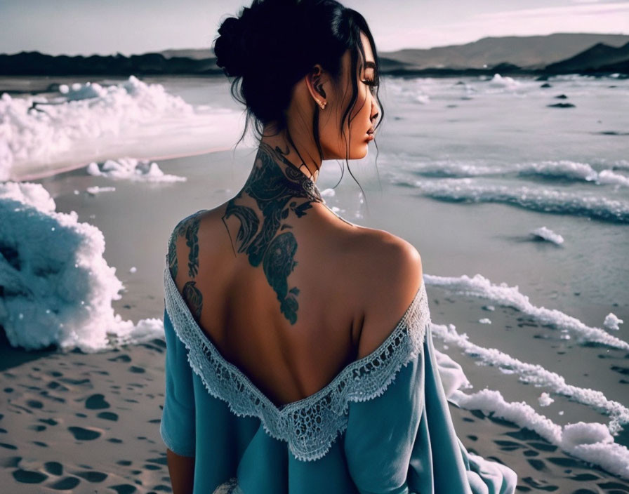 Woman with back tattoo in blue off-shoulder top by the sea