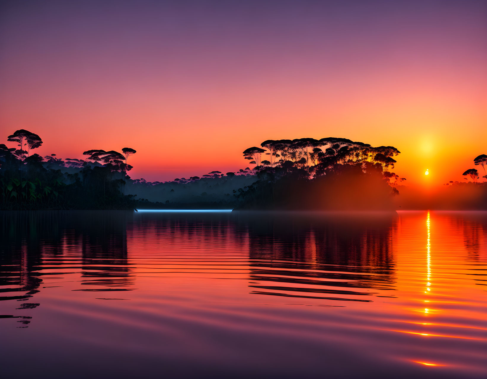 Vibrant pink and orange sunset over still lake and tree silhouettes