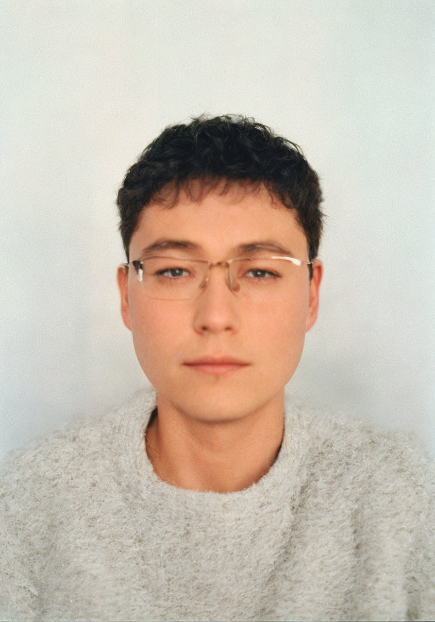 Portrait of Young Man with Curly Hair and Glasses in Textured Sweater