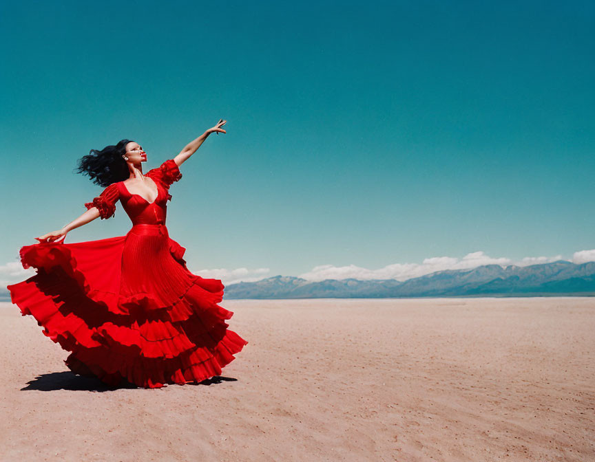 Woman in flowing red dress dancing on barren desert plain with mountains in the distance