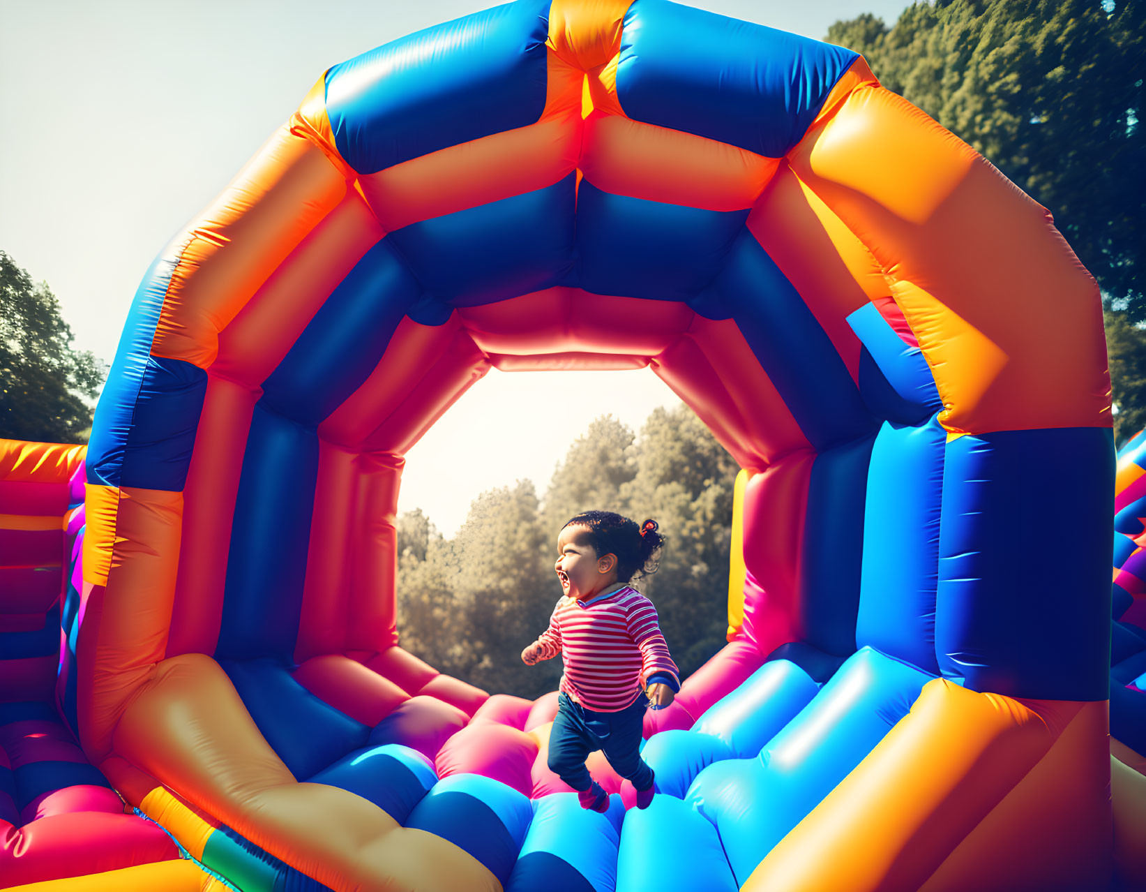 Cheerful toddler with ponytail playing in colorful bounce house