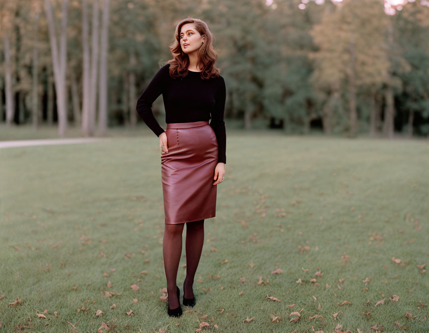 Woman in black top and brown skirt in grassy field with autumn leaves and trees