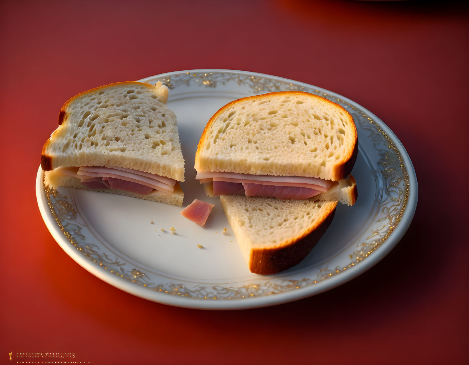 Ham Sandwich Halved on White Plate with Gold Trim on Warm Orange Background