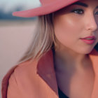 Woman in pink hat and coat with subtle makeup, serene expression at dusk