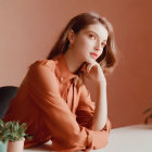 Woman with red lipstick in terracotta blouse against matching background.