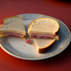 Ham Sandwich Halved on White Plate with Gold Trim on Warm Orange Background