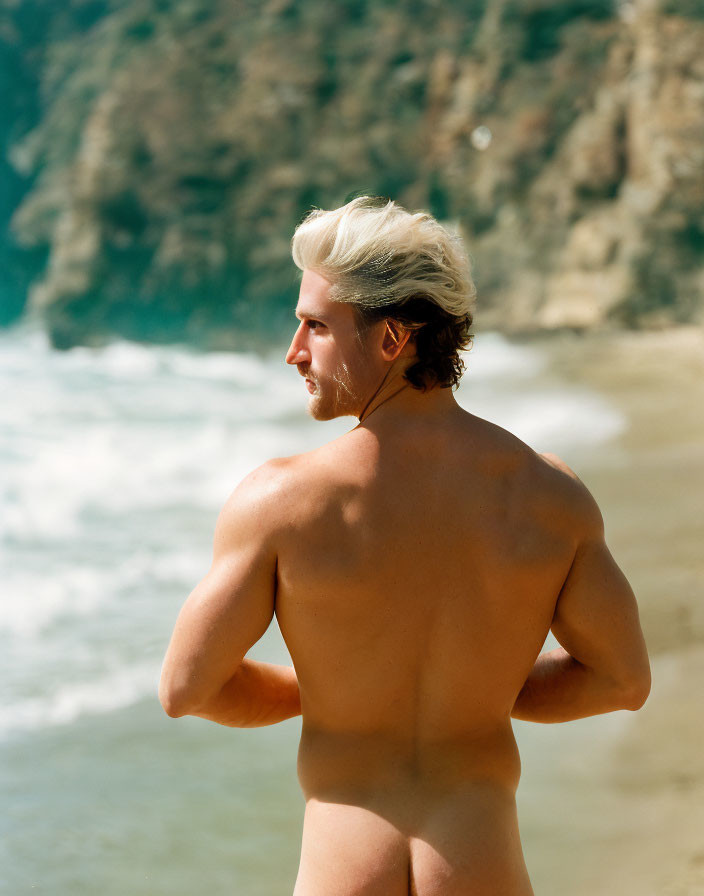 Blond man on sandy beach with cliffs in background