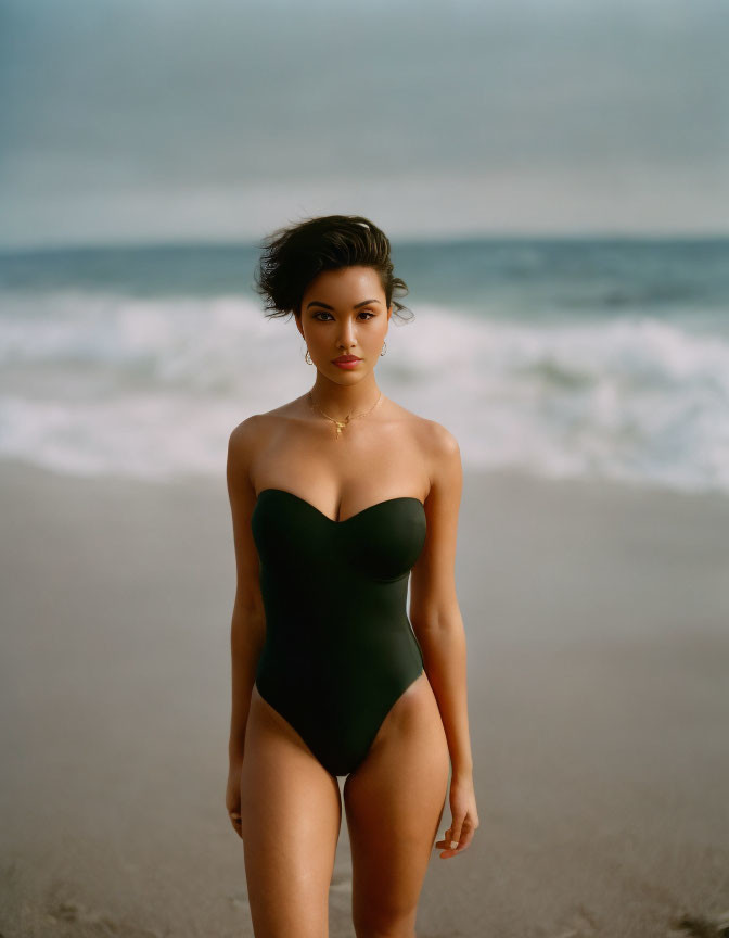 Woman in Black Swimsuit on Beach with Waves and Styled Hair