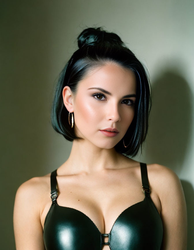 Dark-haired woman in bun and hoop earrings against neutral backdrop