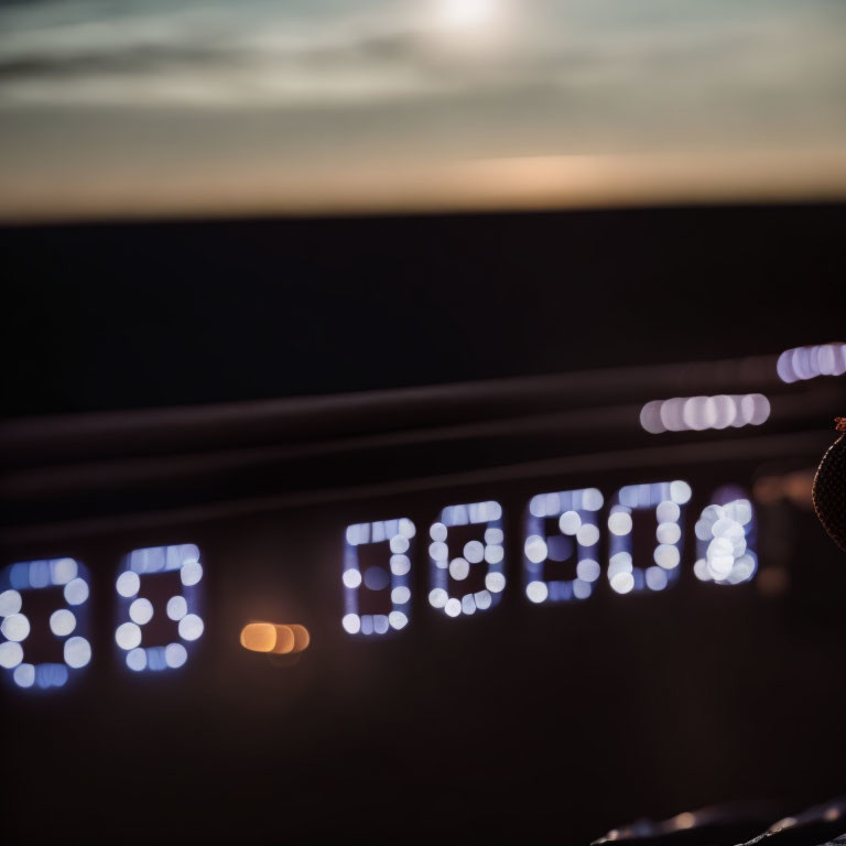 Car dashboard digital clock at dusk with 10:10 time and sunset backdrop