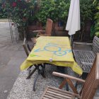 Solitary figure at elegantly set outdoor table with yellow tablecloth, surrounded by plants and umbrella.