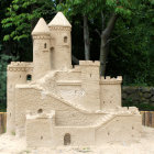 Detailed sandcastle with multiple towers and turrets against lush green trees