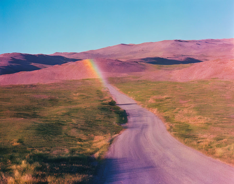 Tranquil landscape with winding road, rolling hills, and rainbow